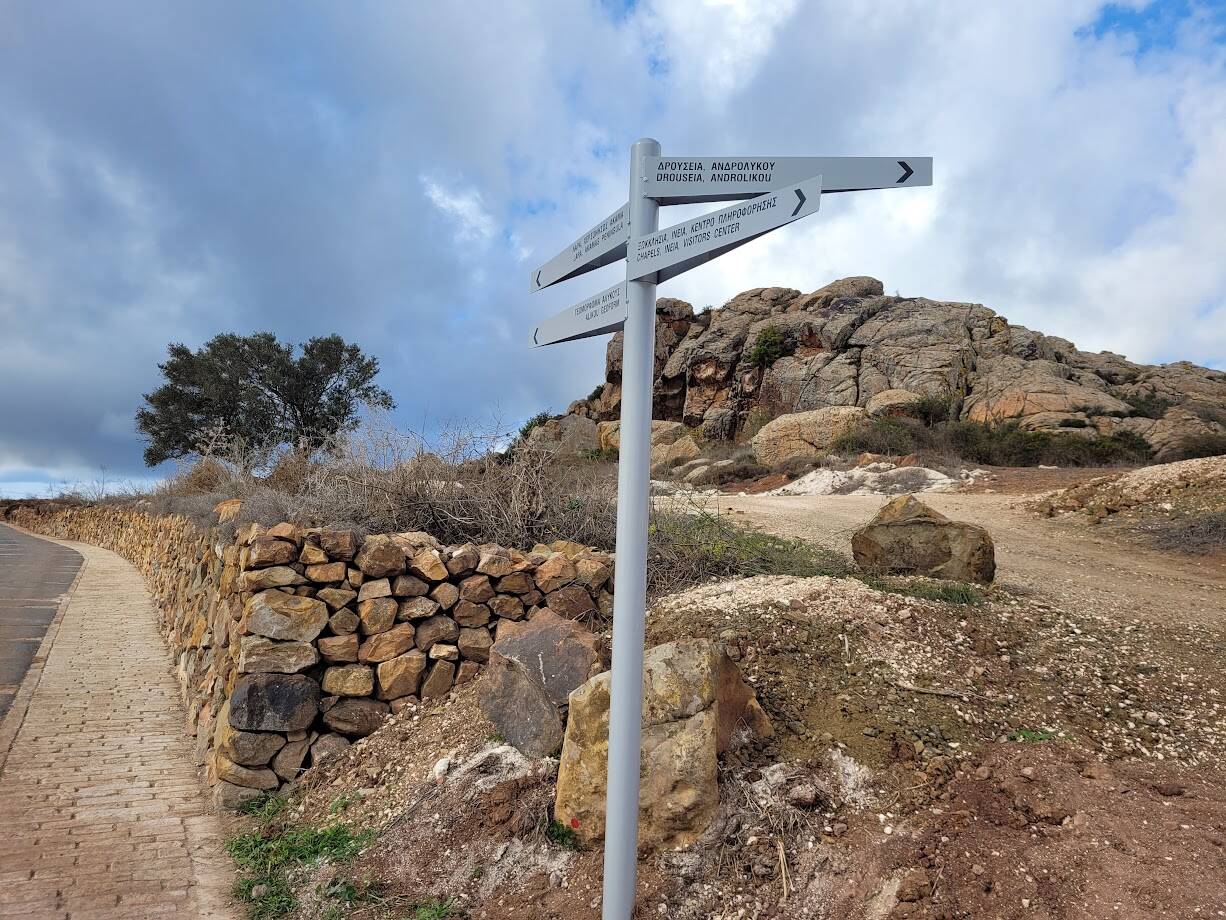 road signs with dry stone wall and an olive tree in the background